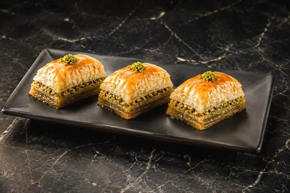 Drei goldbraune Pistazien-Baklava auf einer schwarzen Platte